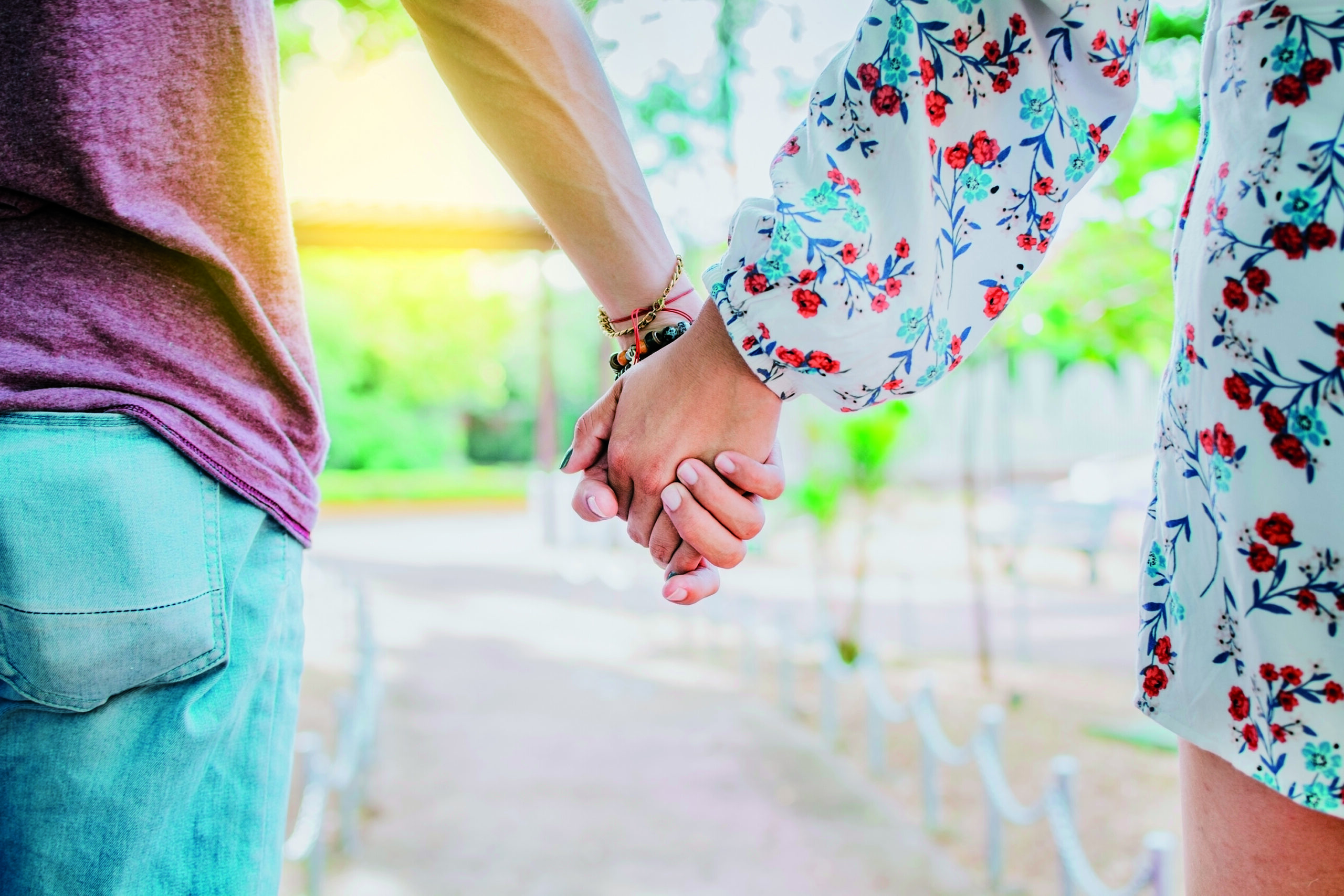 Close up of couple holding hands outdoors, Close up of young couple walking holding hands. Close-up of teenagers holding hands in a park. View of young couple holding hands outdoors